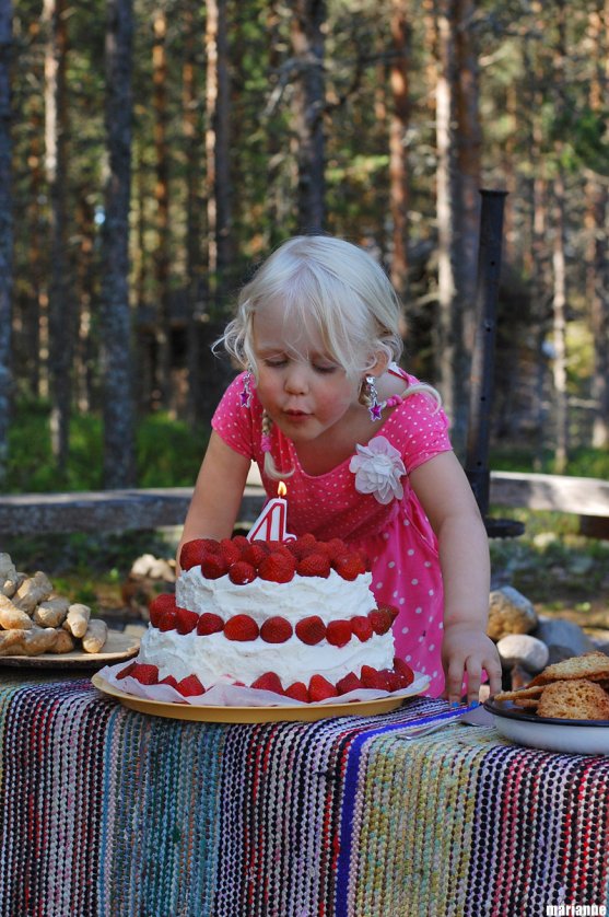 child-blowing-candles-from-her-strawberry-cake-in-summer