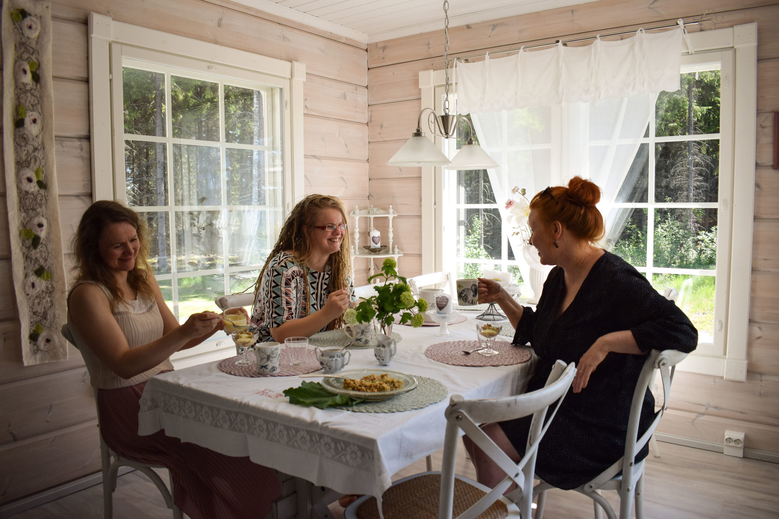 three women sitting at the table in lakeside cottage of hienosen lomamökit